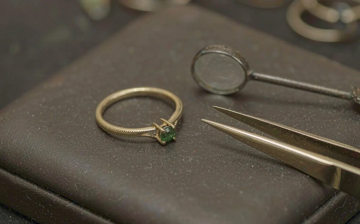 Ring with a green gemstone being worked on with a loupe and tweezers