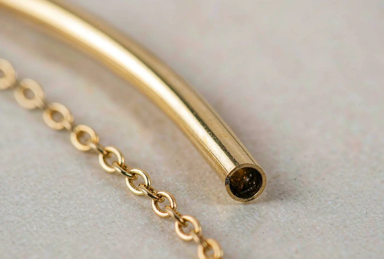 Extreme close-up of a thin hollow gold tube and an openwork gold chain showing the hollow lightweight structure