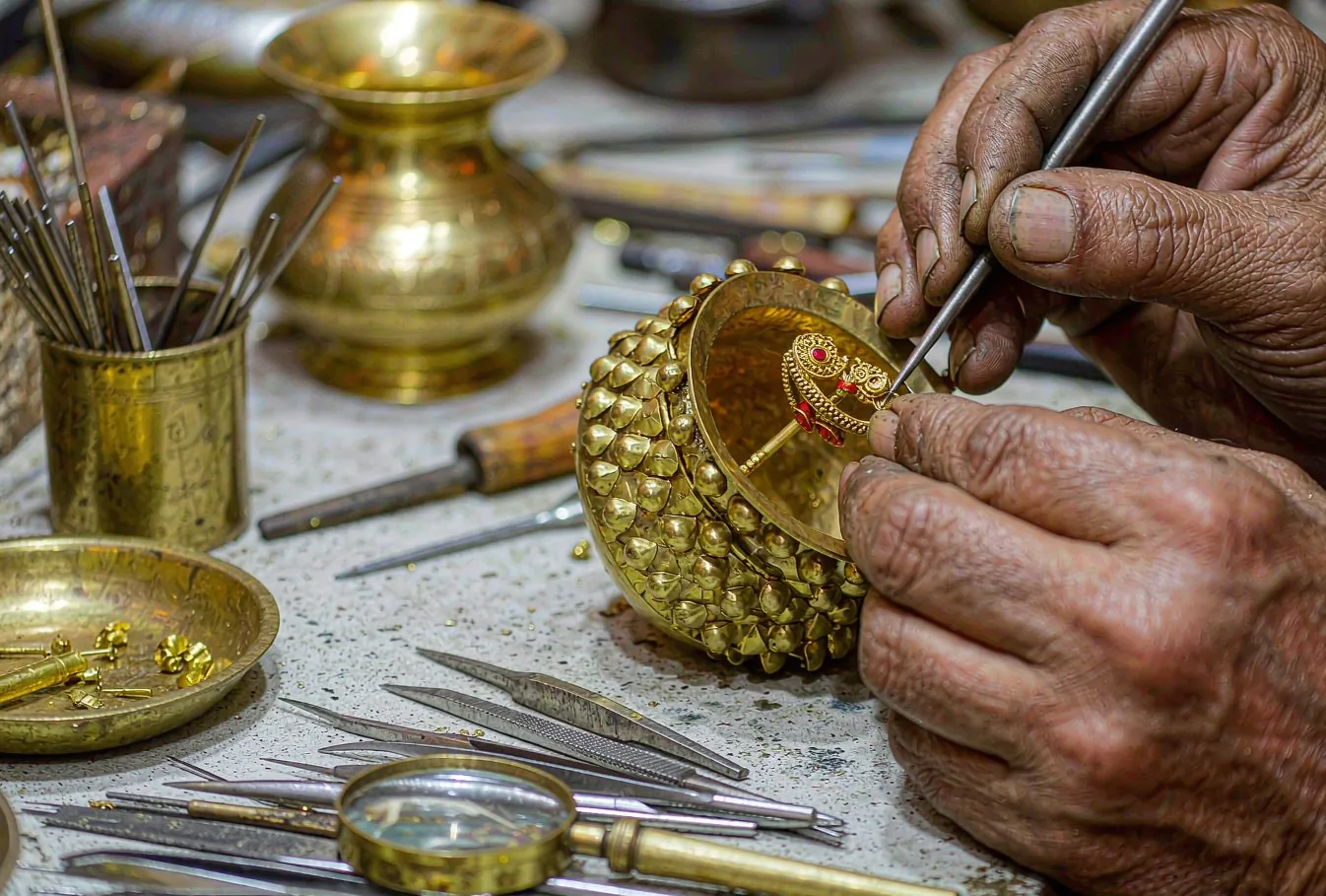 An Indian goldsmith's hands working a small gold ornament with fine tools at a workshop bench