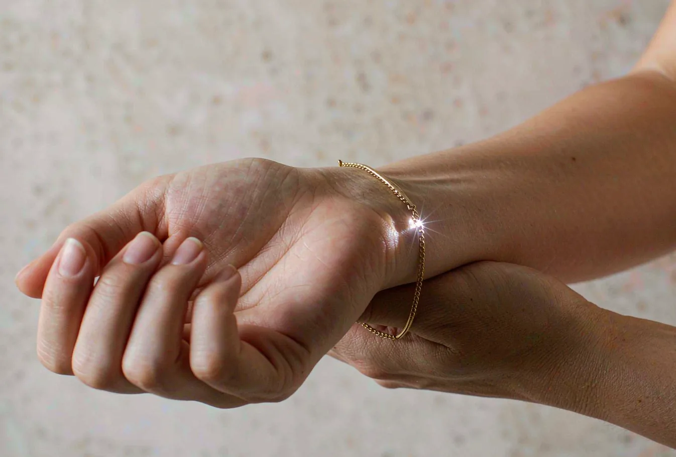 A fine gold chain bracelet being welded closed on a wrist, with a small weld spark at the join